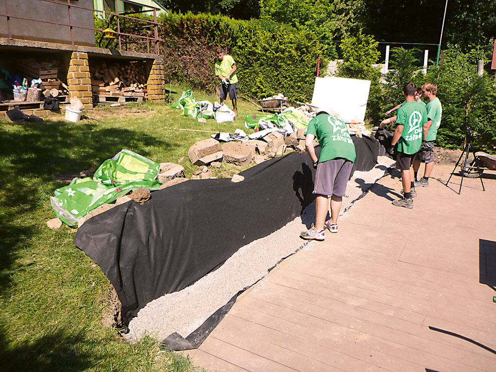 Drenážna vrstva. Do ryhy vysypte jemný makadam až po okraj palubovky. Roztiahnite ho po celej dĺžke múrika a zarovnajte hrabľami.