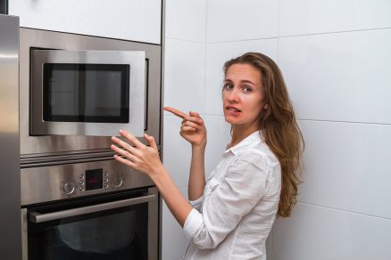 Žena stojaca pri otvorenej mikrovlnke sklamane pozerá a ukazuje na výsledok varenia